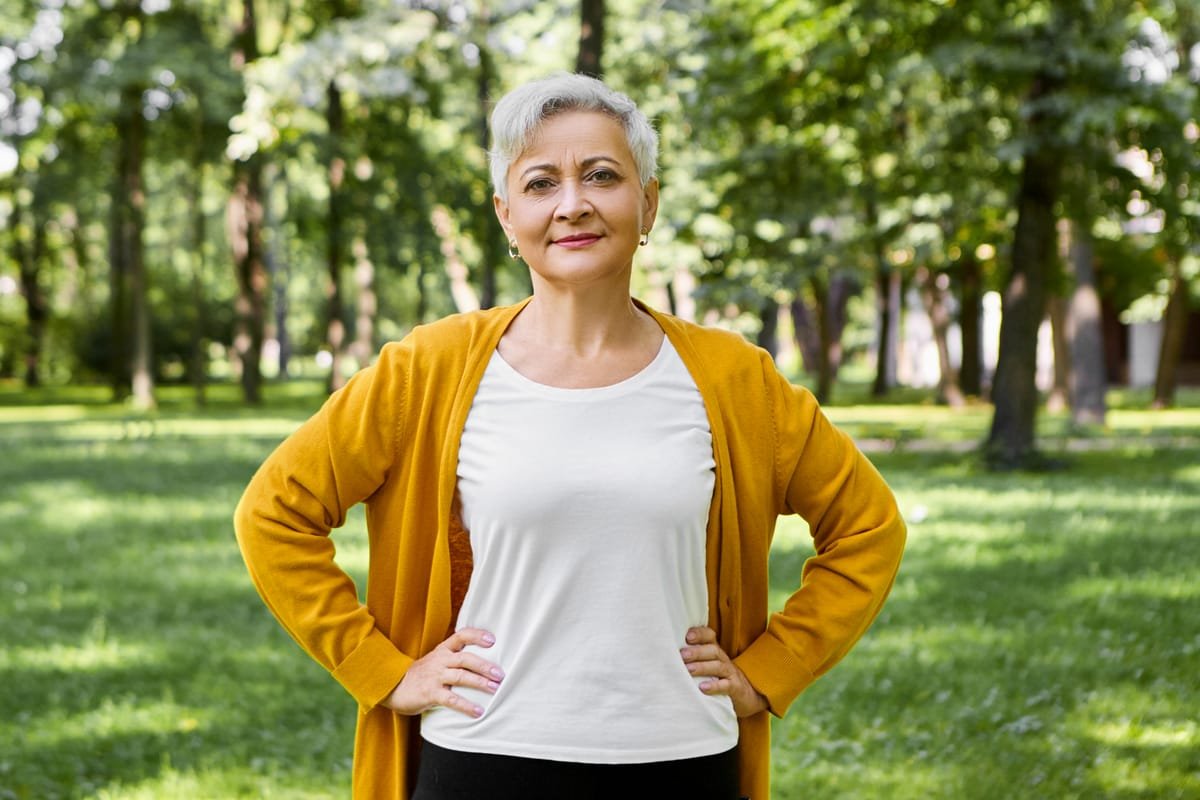 Femme aux cheveux gris souriant avec assurance dans un parc en été
