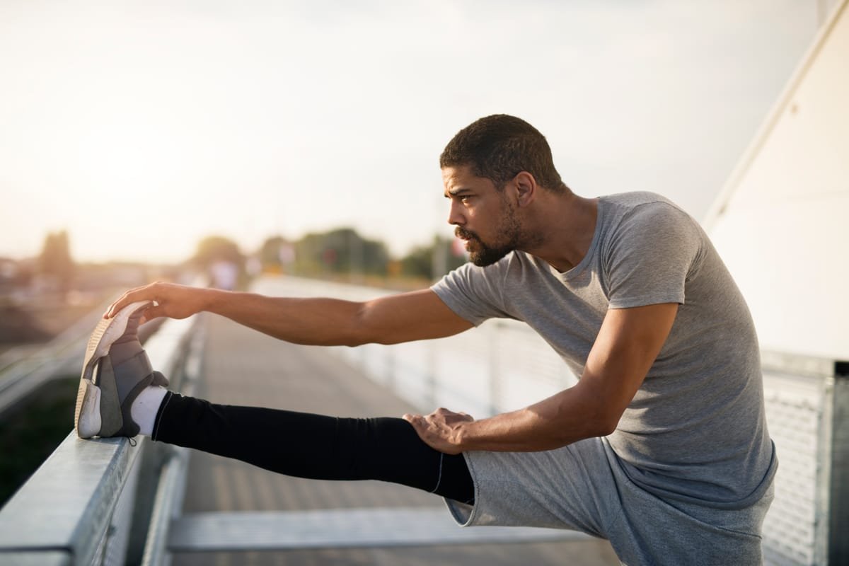 Sportif qui s’étire les jambes au coucher du soleil avant d’aller courir